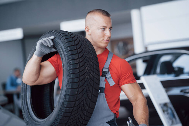 Mechanic holding a tire tire at the repair garage. replacement of winter and summer tires. - Foto, imagen