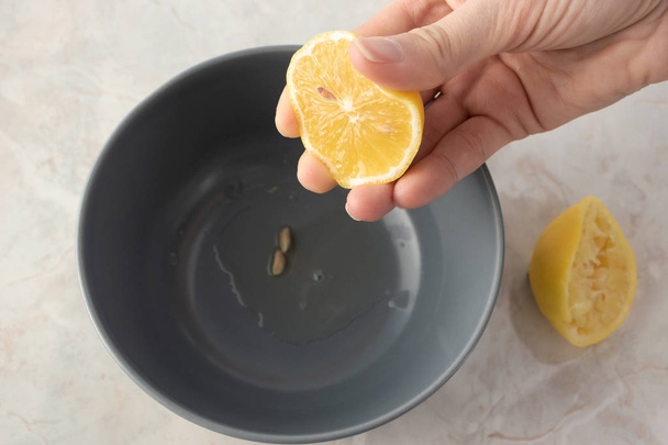 Hand holding half of lemon over gray bowl with juice on marble t - Foto, Imagem