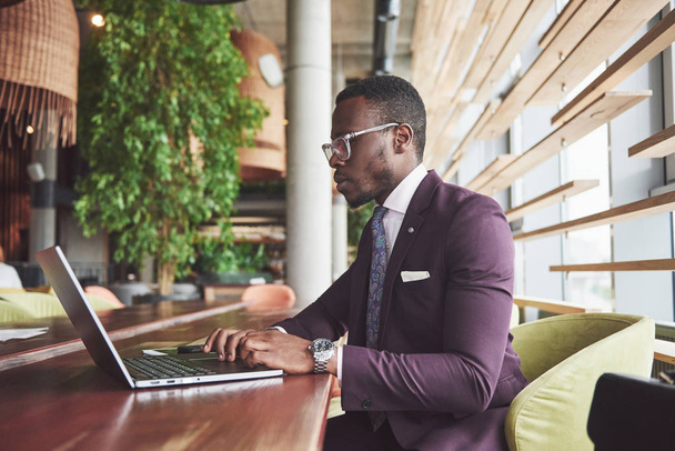 A beautiful stylish African American businesswoman wearing a suit uses his laptop while working. - Zdjęcie, obraz
