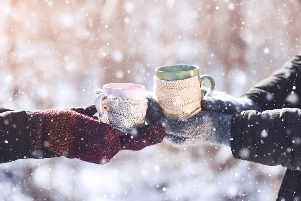 Couple hands in mittens take a mugs with hot tea in winter park. - Foto, Imagem