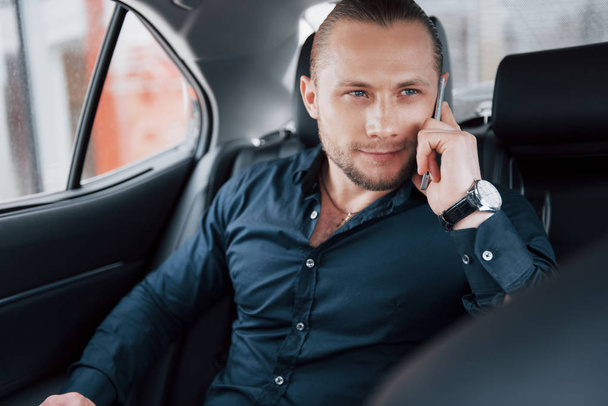A modern businessman speaks on the phone in the back of the car. - Foto, afbeelding