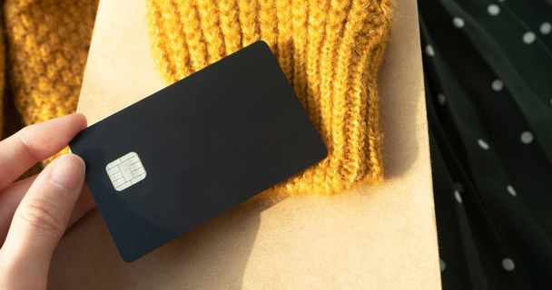 Mano sostiene tarjeta de crédito de plástico negro en lana amarilla tejer swe
 - Foto, Imagen