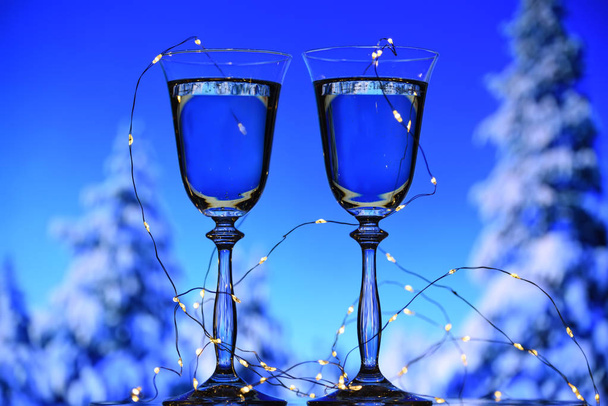 Dwa kieliszki musującego wina szampana i girlanda ze światłami na tle zimowego lasu w śniegu. Zimowy nastrój zimowych wakacji. - Zdjęcie, obraz