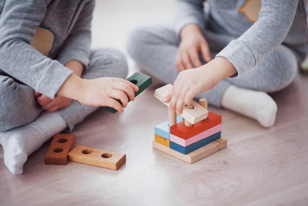 Children play with a toy designer on the floor of the children's room. Two kids playing with colorful blocks. Kindergarten educational games. Close up view. - 写真・画像