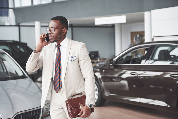 Young black businessman on auto salon background. Car sale and rent concept. - Foto, Bild