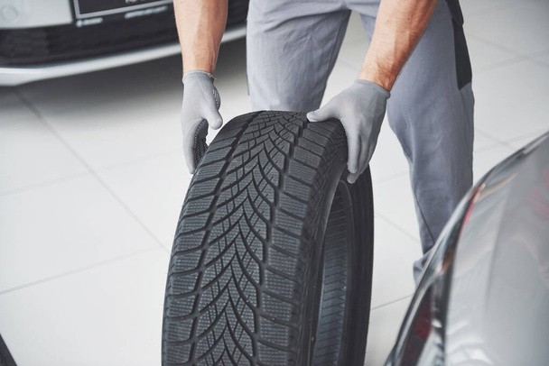 Mechanic holding a tire tire at the repair garage. replacement of winter and summer tires. - 写真・画像