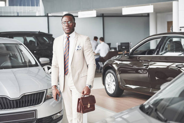 Young black businessman on auto salon background. Car sale and rent concept. - Foto, afbeelding