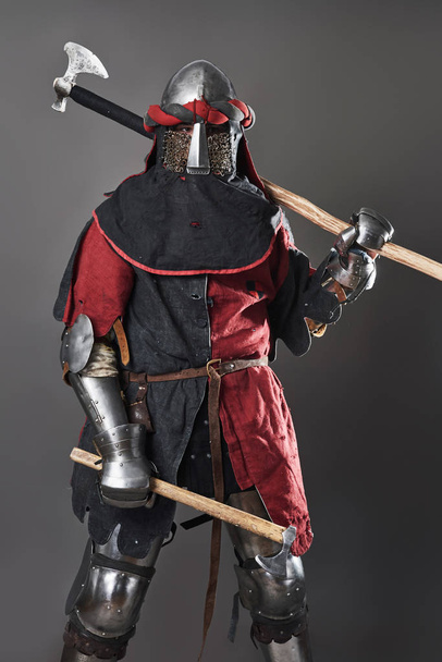Medieval knight on grey background. Portrait of brutal dirty face warrior with chain mail armour red and black clothes and battle axe. - Foto, immagini