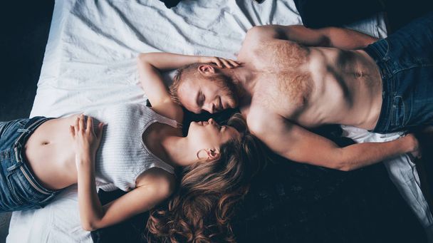 A portrait of a happy young couple who relax in a cozy bed. - 写真・画像
