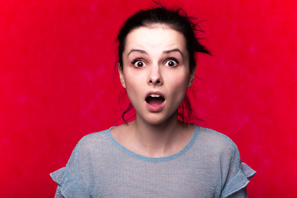 όμορφη συναισθηματική κοπέλα σε ένα t-shirt σε ένα κόκκινο φόντο - Φωτογραφία, εικόνα