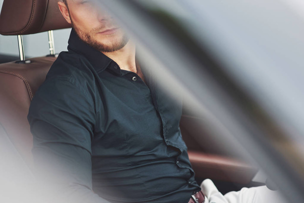 Beautiful young man in full suit while driving a car. - Zdjęcie, obraz