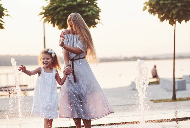 There is no too much water at this season. In a hot sunny day mother and her daughter decide to use fountain for cooling themselves and have fun with it. - Foto, afbeelding