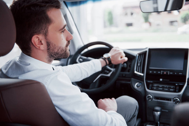 Rear view of confident young businessman sitting at the wheel of his new car. - 写真・画像