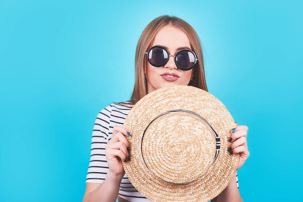 Attractive girl in a white and black stripes, hat, sunglasses, emotionally opened mouth on a bright blue background with a perfect body. Isolated. Studio shot. - Foto, imagen
