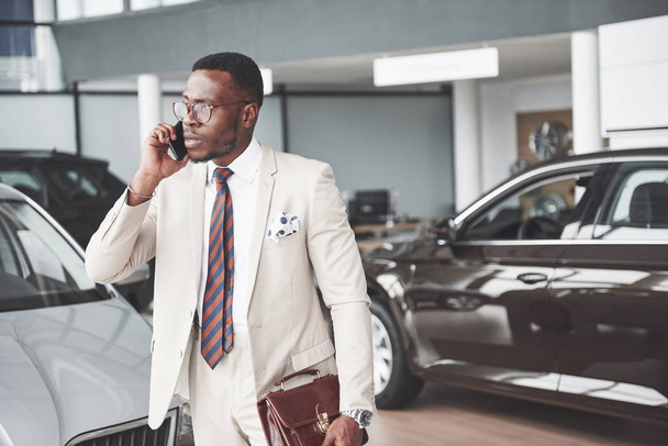 Young black businessman on auto salon background. Car sale and rent concept. - Foto, Imagem