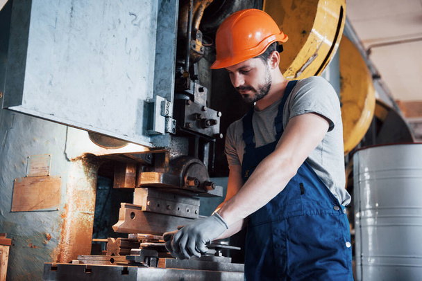 Portret van een jonge arbeider met een harde hoed in een grote metaalfabriek. De ingenieur bedient de machines en vervaardigt onderdelen voor gasapparatuur. - Foto, afbeelding