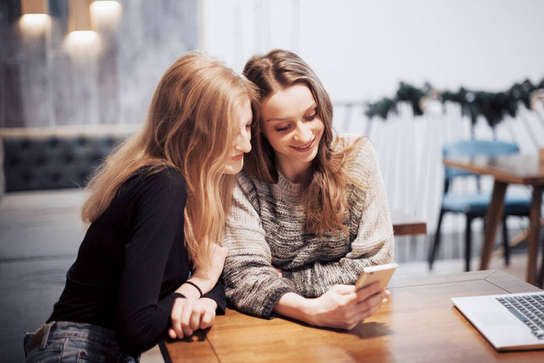 One-on-one meeting.Two young business women sitting at table in cafe.Girl shows her friend image on screen of smartphone. On table is closed notebook.Meeting friends. - Foto, Bild