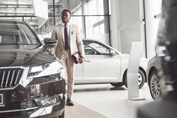 Young black businessman on auto salon background. Car sale and rent concept. Rich african american man. - Fotó, kép