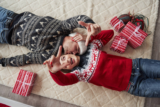 Hands in the air. Top view of couple in Christmas clothes lies on the floor with gifts on it. - Foto, Imagem