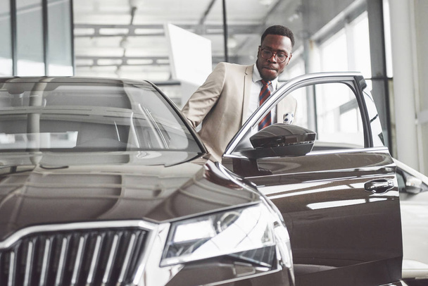 Young black businessman on auto salon background. Car sale and rent concept. Rich african american man. - Fotografie, Obrázek