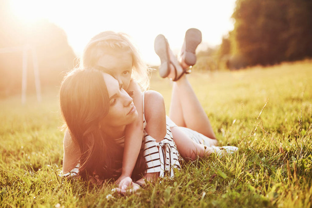 Happy mother and daughter hugging in a park in the sun on a bright summer background of herbs - Photo, image