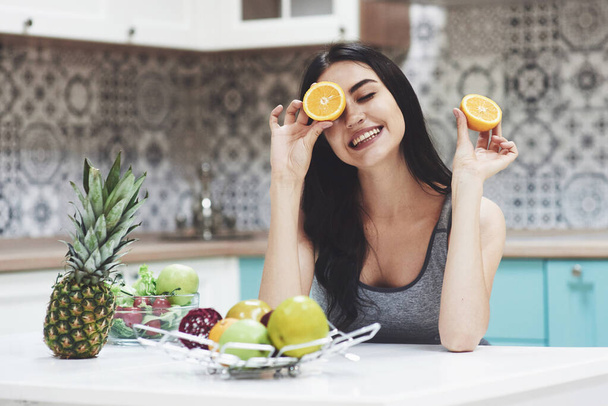 A young sports girl enjoys a fruit salad. Being playful covering her eyes with orange. - Foto, Imagem