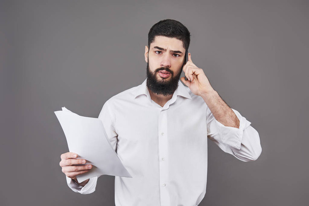 Business man with beard in white shirt holding documents and phone on gray background. - Fotoğraf, Görsel