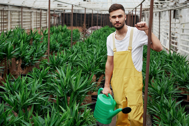 Photo of bearded young man in the greenhouse and holding water canister. - Photo, Image