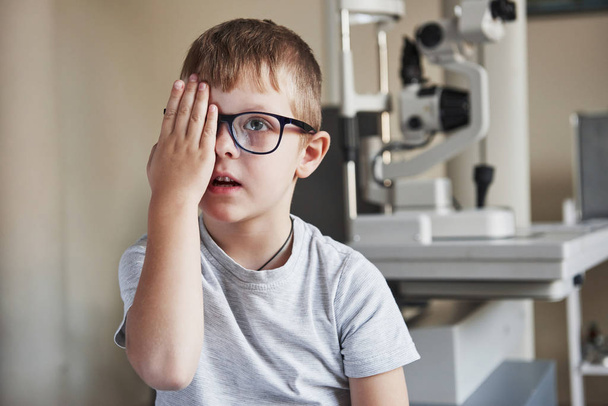 Concentrating on images. Little boy covering his eye and have reviewing eyesight in the clinic. - Foto, Imagen