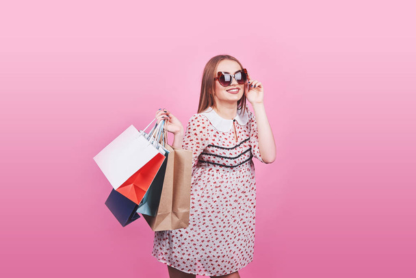Portrét mladé šťastné usměvavé ženy s nákupními taškami na růžovém pozadí. - Fotografie, Obrázek