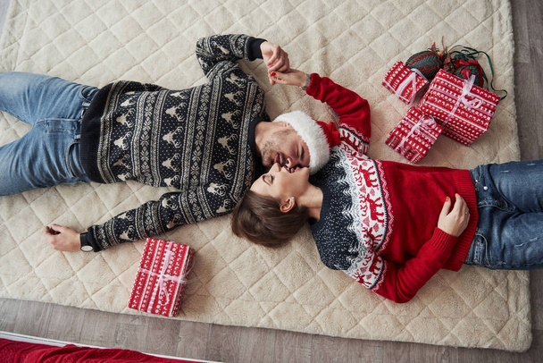 Top view of couple in Christmas clothes lies on the floor with gifts on it. - Фото, зображення