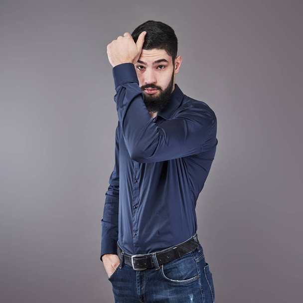 Handsome young bearded man is looking away while standing against gray background. - Photo, Image