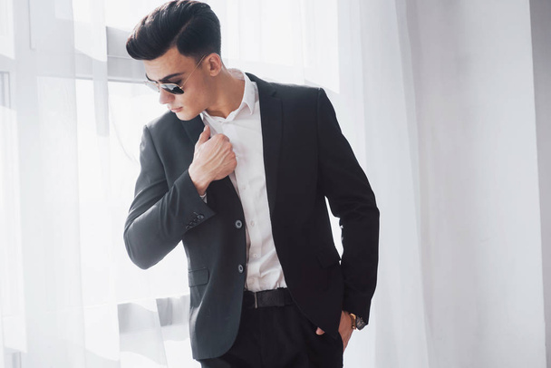 A fashionable hairstyle stands out. Portrait of young stylish man in classic business wear standing in the white room. - Photo, Image