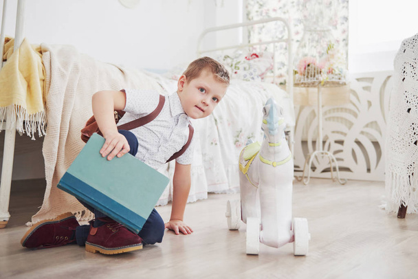 Cute little boy is going to school for the first time. Child with bag and book. Kid makes a briefcase, child room on a background. - Foto, afbeelding