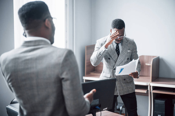 Modern businessman at work. Two confident business people in formalwear discussing something While one of them looks at the documents and the second an important phone call. - Foto, imagen