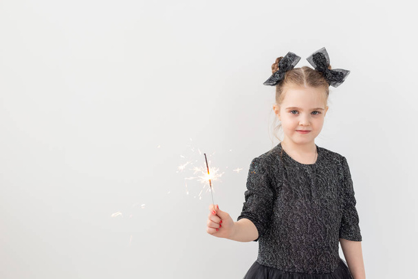 Urlaub, Weihnachten und Neujahr - glückliches Kind hält brennende Wunderkerze in der Hand über weißem Hintergrund mit Kopierraum - Foto, Bild