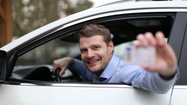 jonge lachende man zit in de auto en toont zijn nieuwe rijbewijs - Video