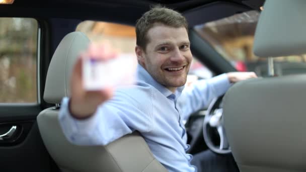 joven feliz hombre sentado en el coche y mostrando su nueva licencia de conducir con el pulgar hacia arriba signo
 - Metraje, vídeo