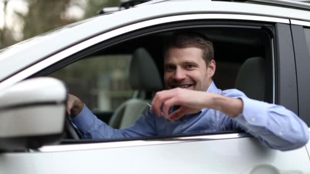 młody człowiek siedzi w samochodzie i pokazuje swoje nowe prawo jazdy z kciukiem w górze znak z okna samochodu - Materiał filmowy, wideo