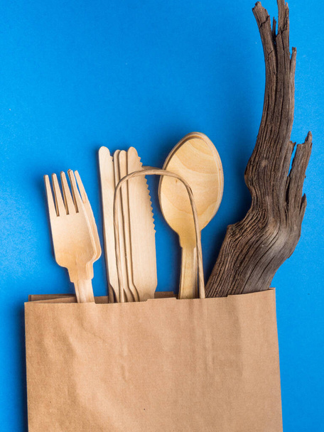 Disposable wooden cutlery in paper bag on trendy blue color background, cutlery, recycling and eco friendly concep, plastic-free alternatives zero waste environmental protection - Photo, Image