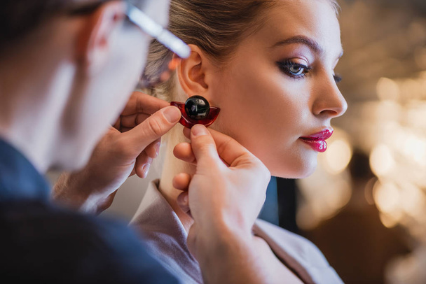 cropped view of stylist putting earring on model on backstage  - Fotografie, Obrázek