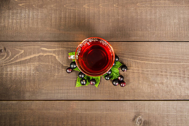 A glass mug of tea with berries of black currant and sugar cubes stands on a birch stump, on a wooden background. - Foto, Imagem