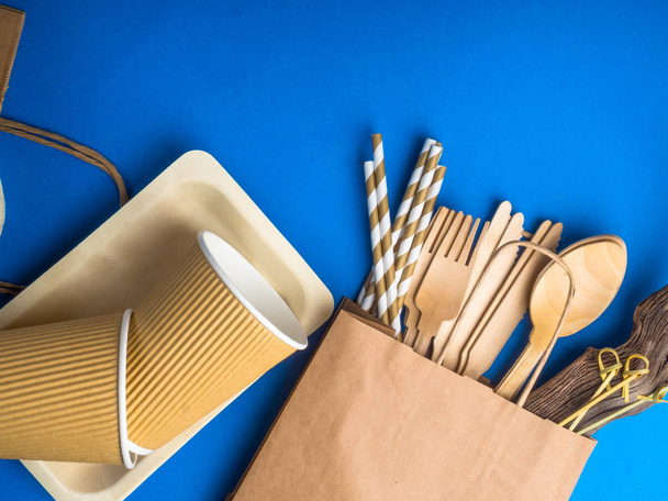 Eco friendly bamboo cutlery set on blue background. Various kraft paper packaging, containers for takeaway food, drinks. Zero waste and recycling concept. - Foto, afbeelding