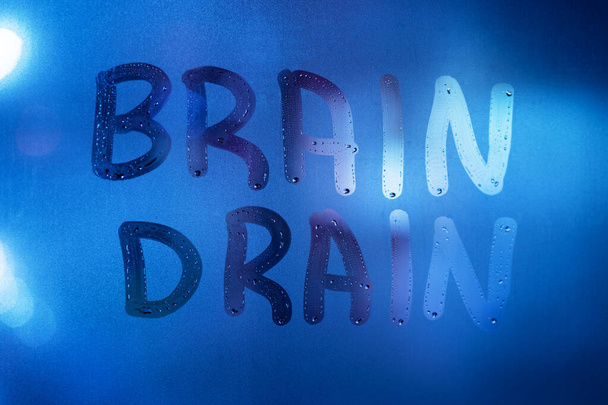 the words brain drain written on night wet window glass close-up with blurred background in classic blue color - Photo, Image