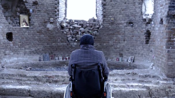 Vista trasera de un hombre en silla de ruedas para discapacitados en la iglesia en ruinas. Filmación. El concepto de pérdida
 - Foto, imagen