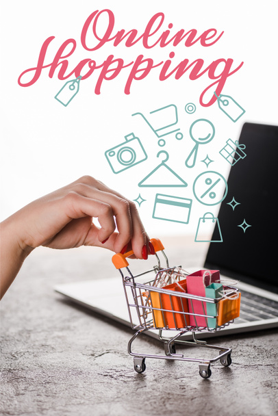 vista cortada da mulher segurando carrinho de compras de brinquedo perto de laptop perto de cartas de compras on-line no branco, conceito de e-commerce
 - Foto, Imagem