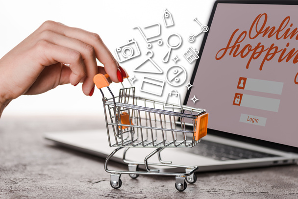 cropped view of woman holding toy shopping cart near laptop with illustration on white, e-commerce concept - Photo, Image