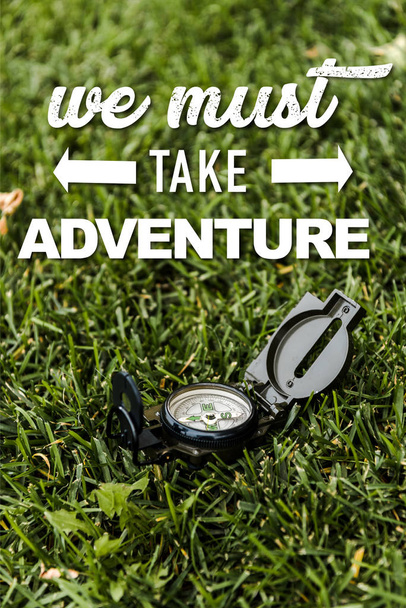 selective focus of black vintage compass on green grass near we must take adventure letters  - Foto, afbeelding