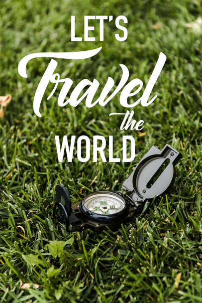 selective focus of black vintage compass on green grass near lets travel the world letters  - Foto, Bild
