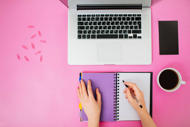 Flatlay with female hands, notebook and laptop. Pink desk. - Foto, imagen